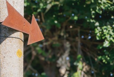 Paslı bir metal ok işareti, gri bir direğe monte edilmiş sol yönü gösteriyor..