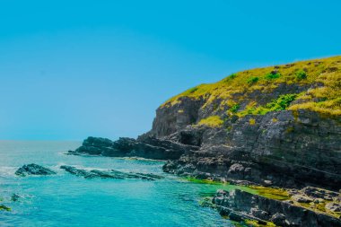 Parlak mavi bir okyanusun üzerinde yemyeşil bitki örtüsüyle süslenmiş engebeli uçurumlar yükseliyor. Parlak gökyüzü, kıyı manzarasının dingin güzelliğini artırıyor. Doğa aşıkları ve kaşifleri için mükemmel..