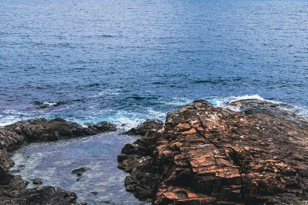 Karanlık, katmanlı kayalar Burgaz yakınlarında Karadeniz 'in mavi sularıyla buluşuyor. Su sakin, bulutlu bir günde kayalık kıyıya vuran dalgalarla birlikte..