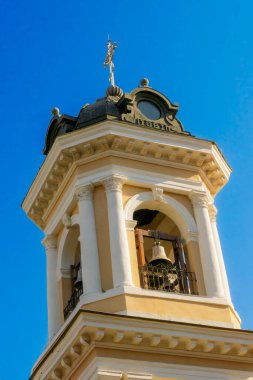 Beyaz sütunları, 1881 yazıtları ve parlak mavi gökyüzüne karşı altın haçı olan tarihi bir kilise çan kulesinin detaylı bir görüntüsü..