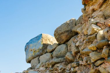 Geniş, yıpranmış kayalar ve pürüzlü dokularla kaplı, açık mavi gökyüzüne tutulan devasa antik taş harabelerin yakın çekimi..