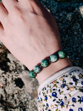 Yeşil yosunlu agla bileziği kadının elinde. Açık havada gri granit yüzeye yakın. Mücevher, aksesuar, sürdürülebilir moda, bohem takılar, boncuklu yeşil bilezik.