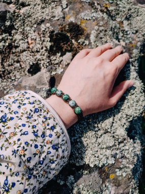 Yeşil yosunlu agla bileziği kadının elinde. Açık havada gri granit yüzeye yakın. Mücevher, aksesuar, sürdürülebilir moda, bohem takılar, boncuklu yeşil bilezik.