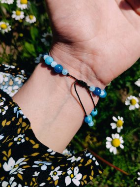  Mavi taşlar, kadının bileğindeki kyanit apatit boncuklu bilezik. Yeşil yapraklar arka plan, güneş ışığı, gölgeler, yaz. Yarı değerli taş makrome ayarlanabilir kilit bilezik, mücevher, aksesuar. 