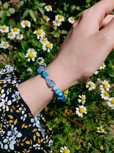 Mavi taşlar kyanit aquamarine apatite. Kadının bileğindeki boncuklu bilezik. Papatya çiçeklerinin arasına yakın. Güneşli bir yaz günü. Yarı değerli taş makrome shamballa bilezik, mücevher, aksesuar, bijouterie