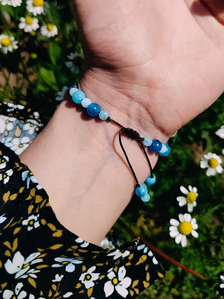  Mavi taşlar, kadının bileğindeki kyanit apatit boncuklu bilezik. Yeşil yapraklar arka plan, güneş ışığı, gölgeler, yaz. Yarı değerli taş makrome ayarlanabilir kilit bilezik, mücevher, aksesuar. 