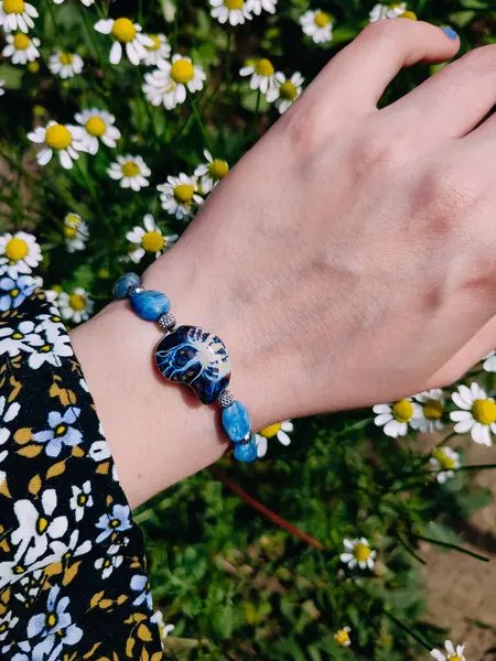 Mavi taşlar kyanit aquamarine apatite. Kadının bileğindeki boncuklu bilezik. Papatya çiçeklerinin arasına yakın. Güneşli bir yaz günü. Yarı değerli taş makrome shamballa bilezik, mücevher, aksesuar, bijouterie