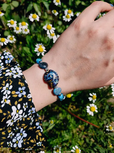 Mavi taşlar kyanit aquamarine apatite. Kadının bileğindeki boncuklu bilezik. Papatya çiçeklerinin arasına yakın. Güneşli bir yaz günü. Yarı değerli taş makrome shamballa bilezik, mücevher, aksesuar, bijouterie