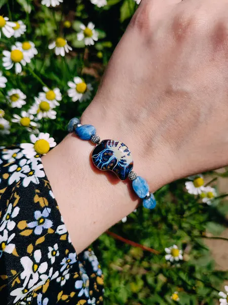 Mavi taşlar kyanit aquamarine apatite. Kadının bileğindeki boncuklu bilezik. Papatya çiçeklerinin arasına yakın. Güneşli bir yaz günü. Yarı değerli taş makrome shamballa bilezik, mücevher, aksesuar, bijouterie