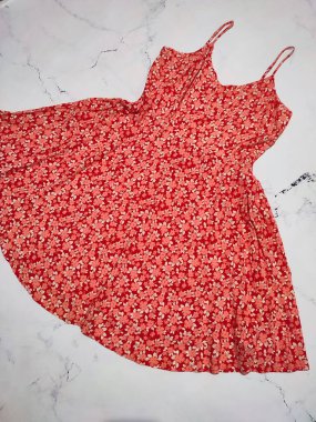 Kırmızı küçük çiçek desenli ince kayışlı kadın elbisesi düz yerde yatıyordu. Beyaz çiçekler, gri mermer arka planda ışıltılı ve parlak bir yaz elbisesi sergilenir. Yaz koleksiyonu, kıyafetler, aşınma, alışveriş, tarz, tasarım