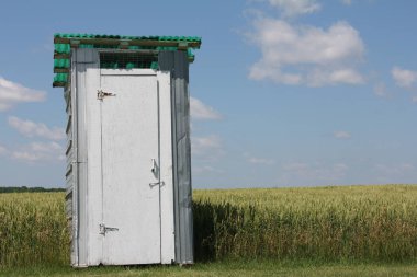 Eski ahşap kapı beyaz kulübe, yeşil çimenlikte ek bina arka planda, mavi gökyüzü