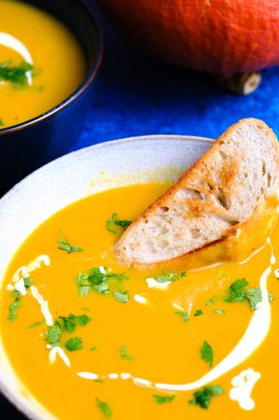 Kabak, balkabağı, taze ekmek ve kremayla süslenmiş mavi zemin üzerindeki balkabağı kreması çorbasını kapat..