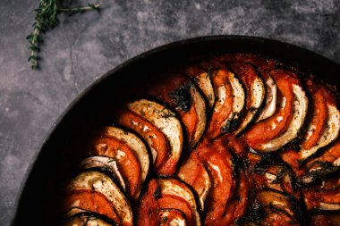 Domatesli Fransız ratatouille, patlıcan, kabak ve koyu arkaplanda dökme demir tavada taze otlar..