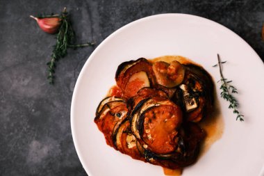 Domatesli Fransız ratatouille, patlıcan, kabak ve koyu arkaplanda dökme demir tavada taze otlar..