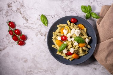 Taze pesto makarna salatası, farklı renkte kiraz domatesleri ve açık arkaplanı olan mozzarella..