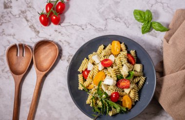 Taze pesto makarna salatası, farklı renkte kiraz domatesleri ve açık arkaplanı olan mozzarella..