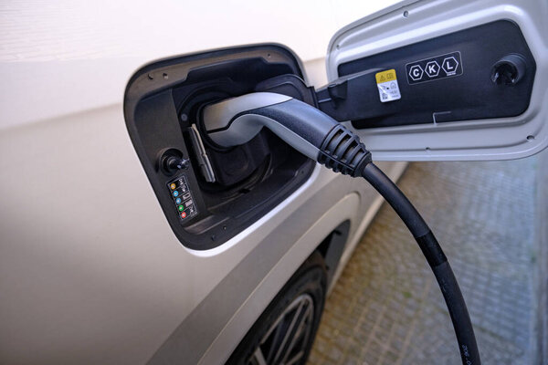 Закрыть кабель зарядки в зарядном порту белой машины. Концепция устойчивого развития электромобилей.