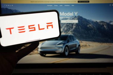 Roosendaal, Hollanda - 10 Şubat 2025: Tesla logosunu gösteren bir cep telefonu, arka plandaki web sitesinde yeni Y Modeli.