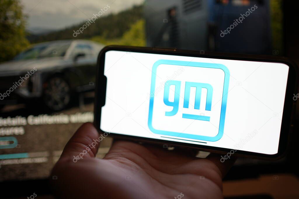 Roosendaal, The Netherlands - February 3, 2025: A phone screen displaying the logo of General Motors, a company that manufactures vehicles. Website with EV in background.