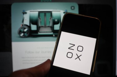 Roosendaal, The Netherlands - February 15, 2025: A mobile phone displaying the logo of Zoox, with the company website in the background. clipart