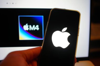Roosendaal, Hollanda - 6 Mart 2025: Apple logosunu gösteren bir cep telefonu, arka planda yeni M4 çipi gösteriliyor.