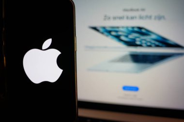 Roosendaal, Hollanda - 6 Mart 2025: Apple logosunu gösteren bir cep telefonu, arka planda M4 çipi olan yeni MacBook Air.