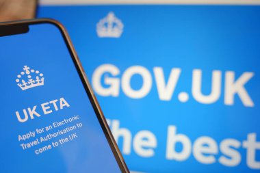 Roosendaal, Hollanda - 2 Nisan 2025: Birleşik Krallık elektronik seyahat iznine başvurmak için bilgili bir cep telefonu. Arkaplanda İngiliz Hükümeti web sitesi.