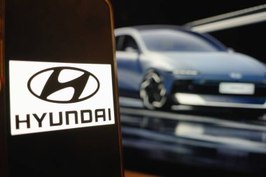 Roosendaal, Hollanda - 6 Nisan 2025: Hyundai logosunu gösteren bir cep telefonu, arka planda Ioniq 6 'nın güncellenmiş ve yüz gerdirilmiş bir resmi.