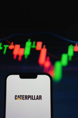 Roosendaal, Hollanda - 05 Ağustos 2025: Caterpillar 'ın şirket logosunu gösteren bir cep telefonu, arkasında da hisse senedi tablosu var. Dikey yönelim.