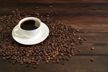 Porselen kahve fincanı ve köpüklü sade kahve. Etrafı bol kavrulmuş kahve çekirdekleri ve ahşap masa.