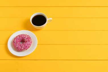 Kahve fincanı ve sarı ahşap arka planda pembe jöleli çörek.