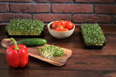 Taze hardal (Brassica juncea) ve turptan (Raphanus sativus) oluşan canlı, ahşap bir masaya yerleştirilmiş ve yanında kırmızı dolmalık biber, salatalık ve olgun domates dolu bir kase..