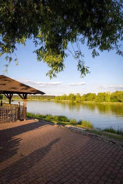 Huzurlu nehir kenarı manzarası, su kenarına giden kaldırım taşı basamakları. Nehrin sakin yüzeyi temiz bir gökyüzünün altındaki yemyeşil ağaçları yansıtır. Rahatlama, seyahat, yaz ve kırsal bölgelerle ilgili kavramlar için idealdir.