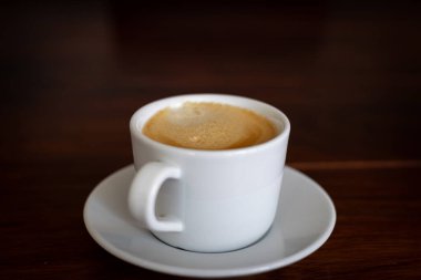 Yeni demlenmiş bir espresso 'nun yakın plan resmi. Beyaz bir porselen bardakta servis ediliyor. Zirvedeki zengin krema ve yumuşak ışıklandırma rahat ve davetkar bir atmosfer yaratıyor. Sabah ritüelleri ve kahve kültürü kavramlarını resmetmek için mükemmel.,