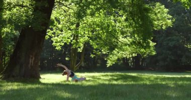 Yalnız kızıl saçlı kız sabahın erken saatlerinde parkta yoga yapıyor. Büyük bir ağacın yanında..