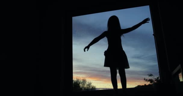 夕阳西下 一个小女孩的侧影在被雨滴覆盖的窗前跳舞 — 图库视频影像