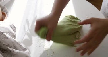 Taze ıspanaktan yapılan canlı yeşil ekmek hamurunu yoğuran ellerin yakın çekimi. Hamur ahşap bir masanın üzerinde duruyor. Bitkisel tarifler, organik yiyecekler ve sanatsal pişirme..