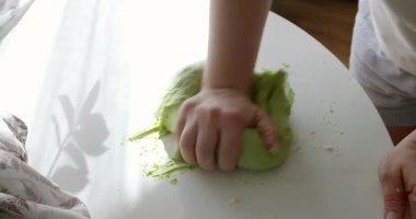 Taze ıspanaktan yapılan canlı yeşil ekmek hamurunu yoğuran ellerin yakın çekimi. Hamur ahşap bir masanın üzerinde duruyor. Doğal yeşil renk, kullanılan besin maddelerine işaret eder..