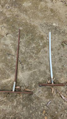 İki paslı, hava yıpranmış metal alet toprak kaplı bir yüzeye uzanıyor, muhtemelen eski bahçıvanlık ya da inşaat aletleri, yıpranma ve yaşlanma belirtileri gösteriyor, dağınık yapraklar terk edilmiş görünüme ekleniyor..