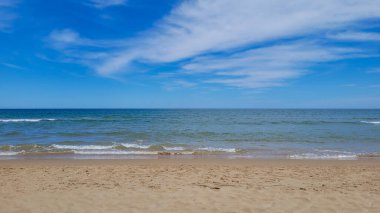 İspanya, Gandia 'da güzel bir Akdeniz plajı. Altın kum, yumuşak okyanus dalgaları ve ince bulutlu açık mavi bir gökyüzü..