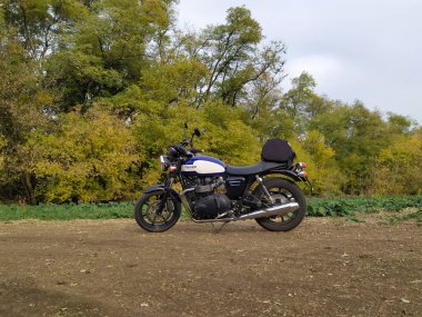 Dnipro, Ukrayna 'da toprak bir yola park edilmiş bir motorsiklet, sonbahar ağaçlarıyla çevrili, barışçıl bir açık hava seti yansıtıyor..