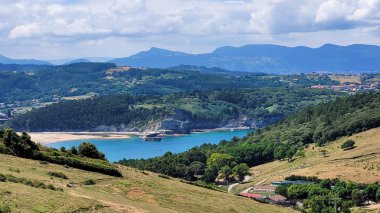 İspanya 'nın Bask Bölgesi' nde yeşil tepeler ve dağlarla çevrili kumlu plajı ve turkuaz suları olan kıyı koyunun detaylı bir görüntüsü..