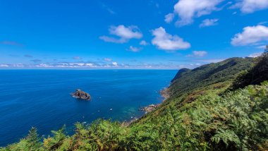 Bereketli yeşil kayalıkların geniş açılı görüntüsü, İspanya 'nın Bask Sahili boyunca derin mavi Atlantik Okyanusu' yla buluşuyor, üzerinde parlak bir gökyüzü var..