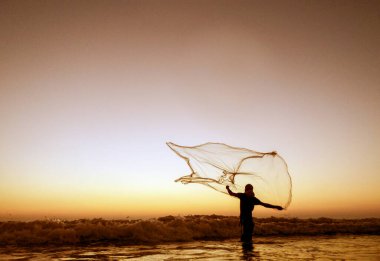 Gün batımında elinde balık ağıyla okyanusta duran bir insanın silueti. Gökyüzü turuncu ve mor sıcak tonlarda boyanarak sakin ve sakin bir atmosfer yaratıyor. Cox 's Bazar, Bengal Körfezi, Bangladeş