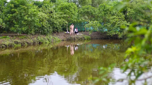 Bangladeş 'te yemyeşil yemyeşil bir gölette balık tutan iki kişi.