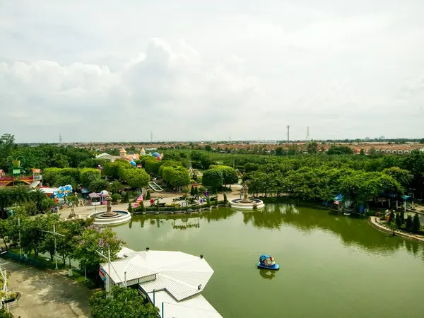 Tayland 'daki Rüya Dünyası eğlence parkının geniş açılı bir görüntüsü. Kürek teknesi, yemyeşil manzarası, büyüleyici binaları ve bulutlu gökyüzü altında park yerleri olan büyük bir gölü gösteriyor..
