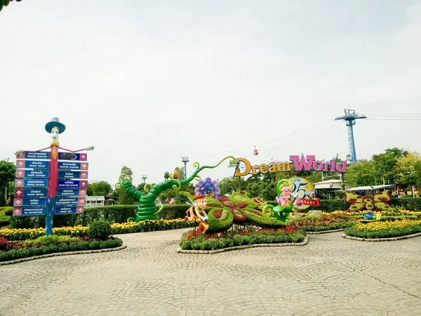 Tayland 'daki Rüya Dünyası eğlence parkının renkli ana giriş alanı, kaprisli ağaç heykelleri, açık bir yön levhası, ve arka planda bir teleferik olan ikonik Rüya Dünyası tabelası.