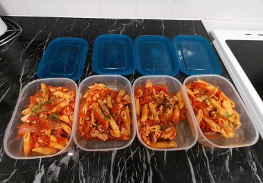 Tavuklu ve domates soslu taze pişmiş makarna. Siyah mermer tezgahta temiz plastik kaplarda depolanmış. Sağlıklı yemek pişirmenin, ev düzeninin ya da yemek hazırlama yaşam tarzının mükemmel bir temsili..