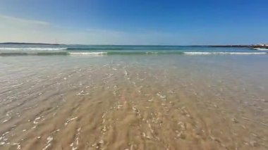 Işıl ışıl mavi bir gökyüzünün altında ışıl ışıl dalgalarla dolu sakin bir sahil manzarası, nihai rahatlama için ideal.