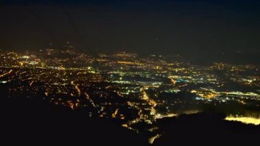 Yüksek dağların nefes kesici perspektifinden canlı şehir ışıklarını gösteren çarpıcı bir gece manzarası.